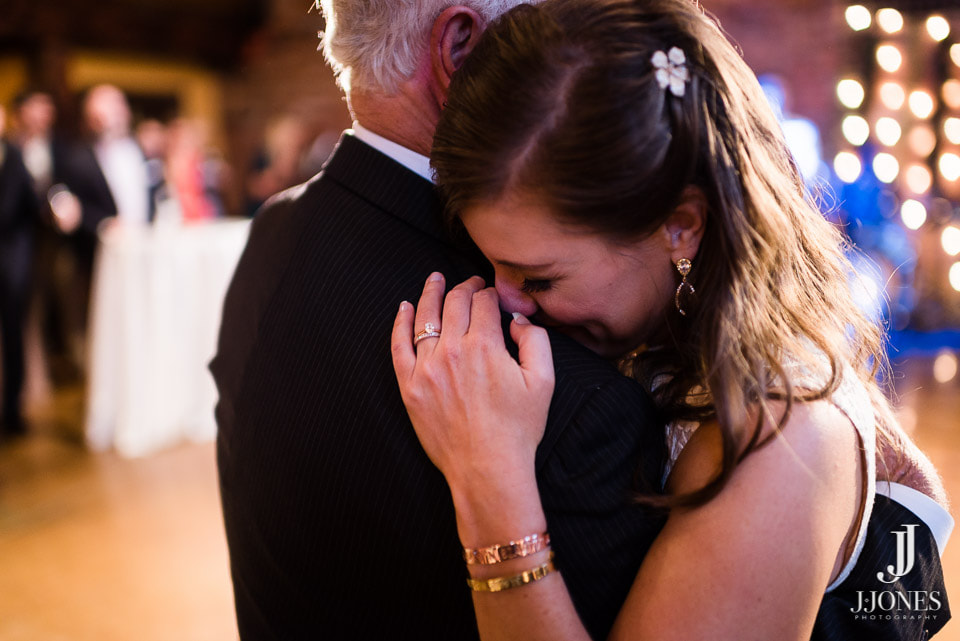 A bride cries happy tears while dancing with her father.