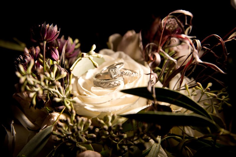 A floral arrangement with wedding bands and engagement ring.