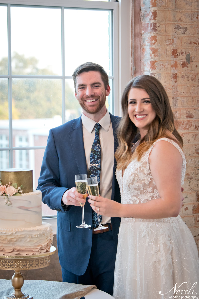 A happy couple shares a champagne toast by their wedding cake