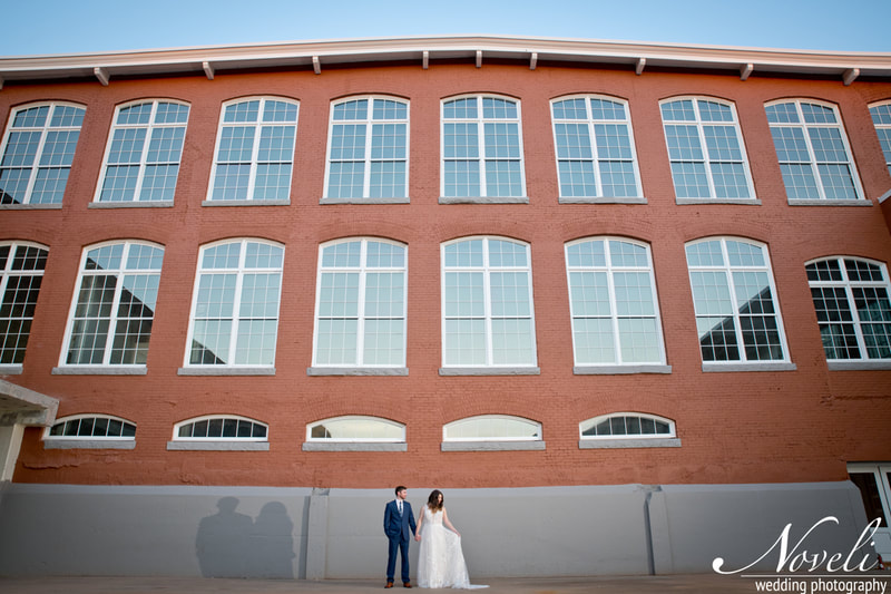 A couple stands against the dramatic backdrop of the Judson Mill lofts
